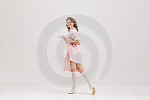 Portrait of young female waitress, sensual woman in retro american fashion style of 70s, 80s in action motion over grey