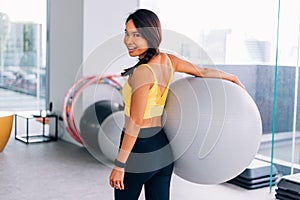 Portrait of young fit Asian woman holding exercise swiss ball and smiling at camera. Lively female fitness model image