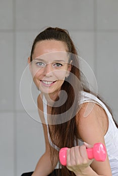 Portrait of young fitness sporty woman in sportswear sitting on fit ball and exercise with dumbbell on gray colour background.