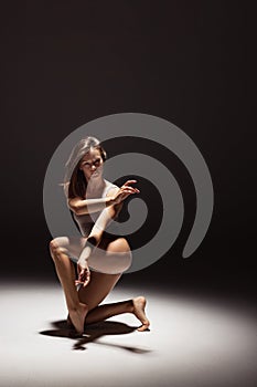 Portrait of young flexible contemp dancer dancing isolated on dark studio background in spotlight. Art, beauty