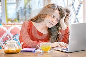 Portrait of young freckled white girl students with long curly red hair working with a laptop