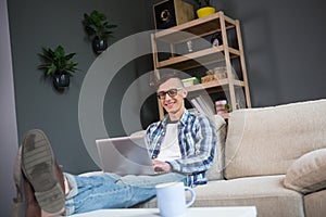 Portrait of young freelancer man sitting on couch keyboarding on laptop.
