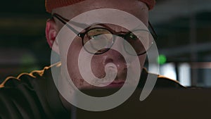 A portrait of a young freelancer in round glasses and a hat in a dark loft cafe