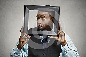 Portrait young funny executive man sticking head in picture frame looking around