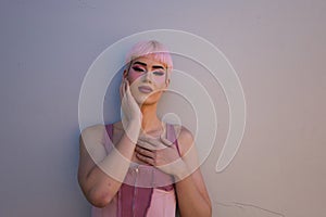 Portrait of young gay boy with pink hair and make-up standing on a white background and making different expressions with his face