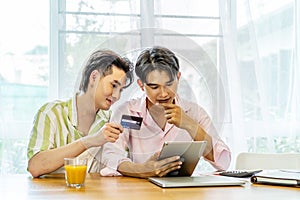 Portrait of young gay couple, lgbt man holding credit card enjoy shopping online with tablet or laptop at home. LGBT and love