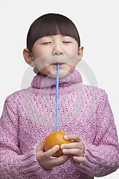 Portrait of young girl with bangs and eyes closed drinking an orange with a straw, studio shot photo