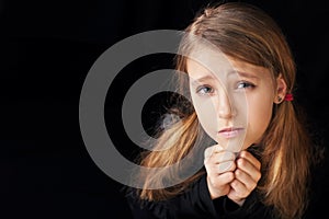 Portrait of a young girl on a black background. She is prayerfully prayed. She asks God for help
