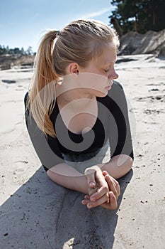 Portrait of young girl in black dress with long blonde hair lying on beach