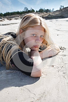 Portrait of young girl in black dress with long blonde hair lying on beach