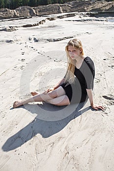 Portrait of young girl in black dress with long blonde hair sitting on beach
