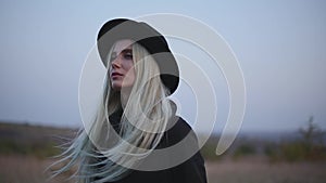 Portrait of young girl with blonde hair, blue eyes, wearing black hat and coat. Background of ultramarine sky.