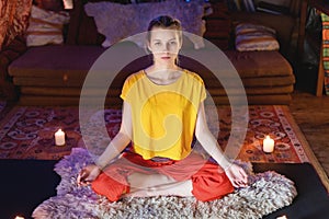 Portrait of a young girl in bright clothes practicing meditation in a crafting room surrounded by candles. Newage