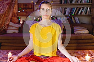 Portrait of a young girl in bright clothes practicing meditation in a crafting room surrounded by candles. Newage