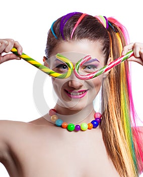 Portrait of a young girl with colorful creative makeup and colored strands of hair. The woman holds in hands colored candy.