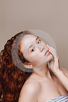 Portrait of a young girl with curly red hair looking at camera on a beige background. Skin Care Concept, Natural Beauty