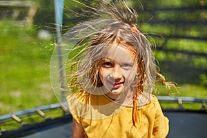 Portrait of young girl with electrified hair on trampoline outdoors, in the backyard