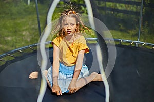 Portrait of young girl with electrified hair on trampoline outdoors, in the backyard