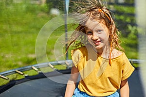 Portrait of young girl with electrified hair on trampoline outdoors, in the backyard