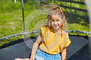 Portrait of young girl with electrified hair on trampoline outdoors, in the backyard