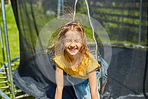 Portrait of young girl on her trampoline outdoors, in the backyard of the house on a sunny summer day