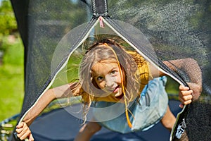 Portrait of young girl on her trampoline outdoors, in the backyard of the house on a sunny summer day