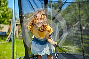 Portrait of young girl on her trampoline outdoors, in the backyard of the house on a sunny summer day