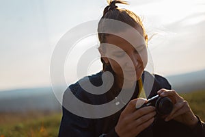 Portrait of young girl holding digital photo camera on background of sunset.