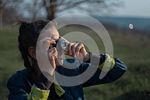 Portrait of young girl holding digital photo camera on background of sunset.