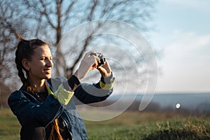 Portrait of young girl holding digital photo camera on background of sunset.