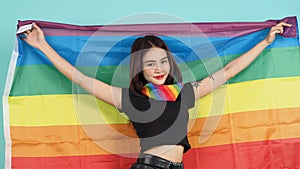 Portrait of young girl holding an LGBT flag standing against a blue green background studio photo