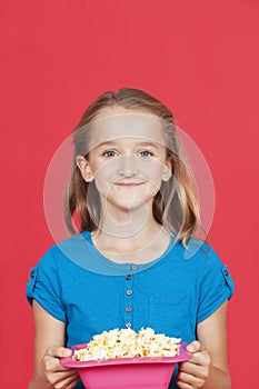 Portrait of young girl holding popcorn container against red background