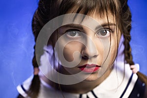 Portrait of a young girl isolated on blue background. Beautiful girl looking at camera. Face gothic child girl. Closeup