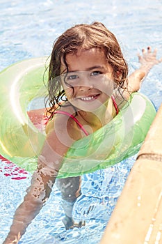 Portrait Of Young Girl Learning To Swim With Inflatable Ring In Swimming Pool On Summer Vacation