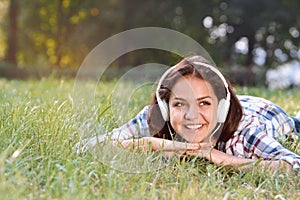 Portrait of young girl listening music lying at the grass