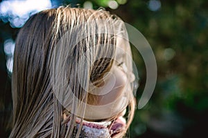 Portrait of a young girl with long blond hair smiling outdoors in a natural setting.