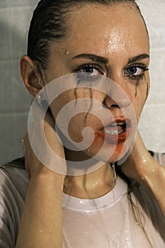 Portrait of a young girl looking at camera with dripping makeup standing in the shower. Vertical Shot