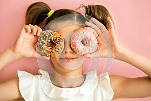 Portrait of young girl looking through two pink donuts, pink background,