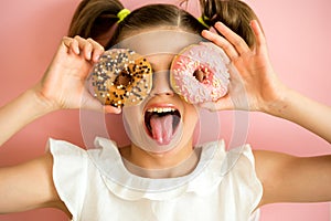 Portrait of young girl looking through two pink donuts, pink background,