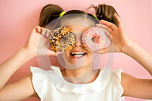 Portrait of young girl looking through two pink donuts, pink background,