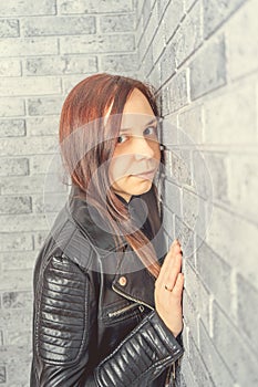 Portrait of a young girl without makeup on her face in a black jacket against a gray brick wall.