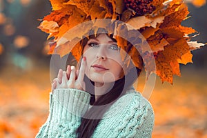 Portrait of a young girl with a maple wreath on her head in an autumn park