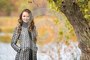 Portrait of a young girl near the tree on a background of autumn river