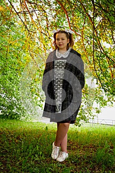Portrait of a young girl in an old school uniform of the USSR with a black dress and a white apron. Teenager in the Park among the