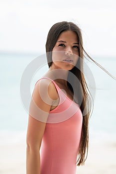 Portrait of a young girl in a pink dress. In the background is a blurry sea and sandy beach
