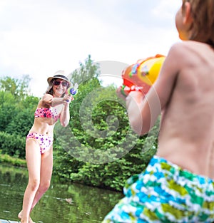 Young girl playing squirt guns with her brother on pier during summer