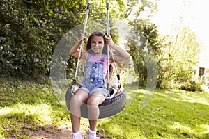 Portrait Of Young Girl Playing On Tire Swing In Garden