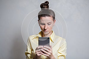 Portrait of young girl playing video games on smartphone, over white background. Dressed in yellow shirt