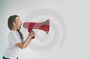 Portrait of young girl shouting using megaphone over background Chil in white shirt, studio shot