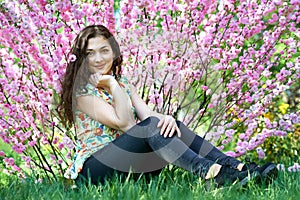 Portrait of young girl sitting near bush with pink flowers